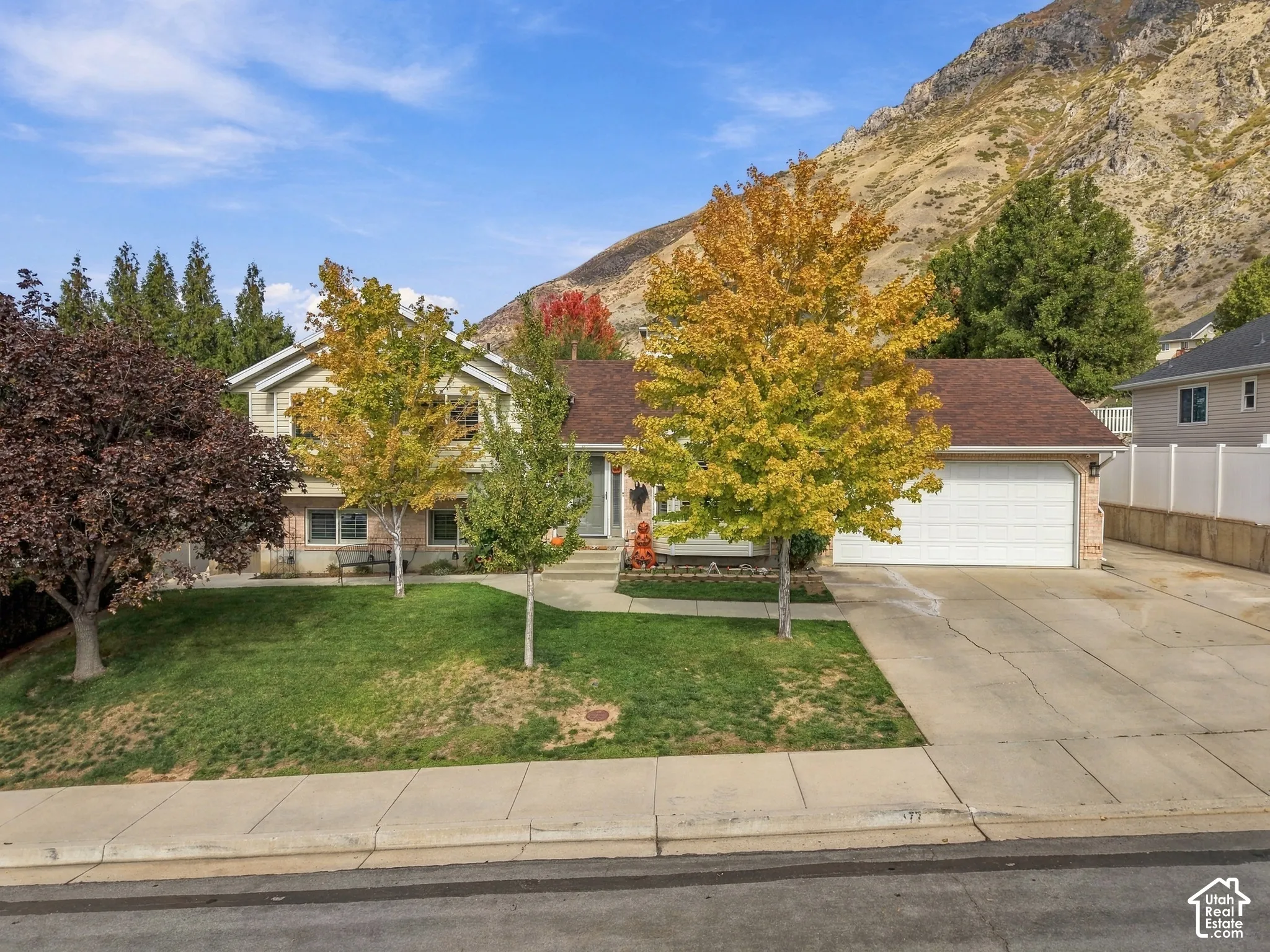 Exterior featuring a multi-level structure with a brick and siding facade, an attached two-car garage, concrete driveway, and mature landscaping set against a mountain backdrop
