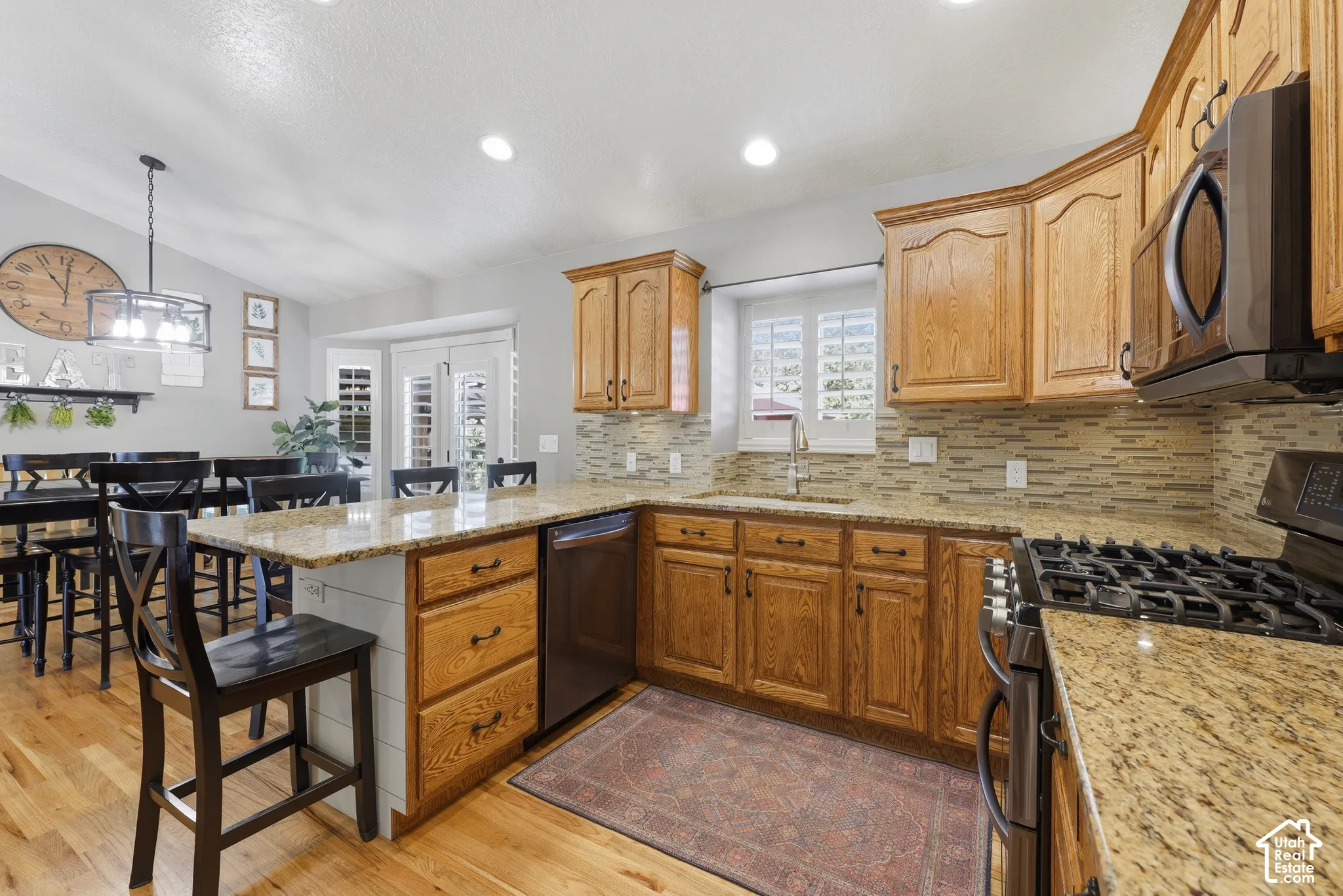 Kitchen featuring natural wood cabinetry, stone-surface countertops, stone-tile backsplash, stainless steel appliances, and wood-finish flooring