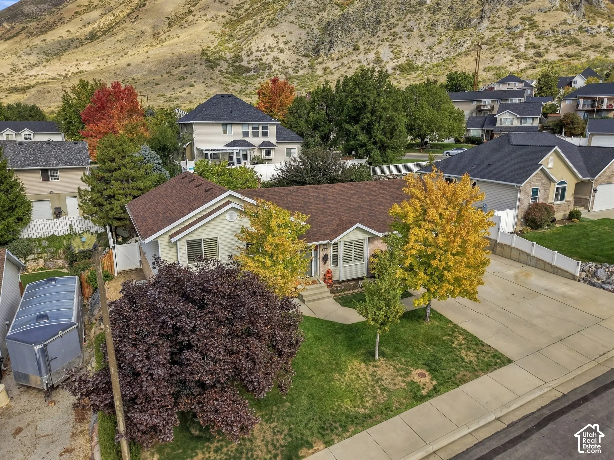 Single-story residence featuring light-toned siding, a multi-gabled shingle roof, concrete driveway, and mature landscaping set against a mountainous backdrop