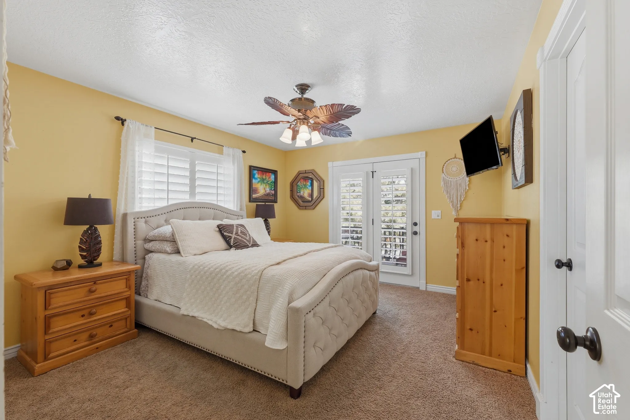 Bedroom featuring neutral carpeting, double glass-panel doors with integrated shutters, and a multi-blade ceiling fan with an integrated light fixture