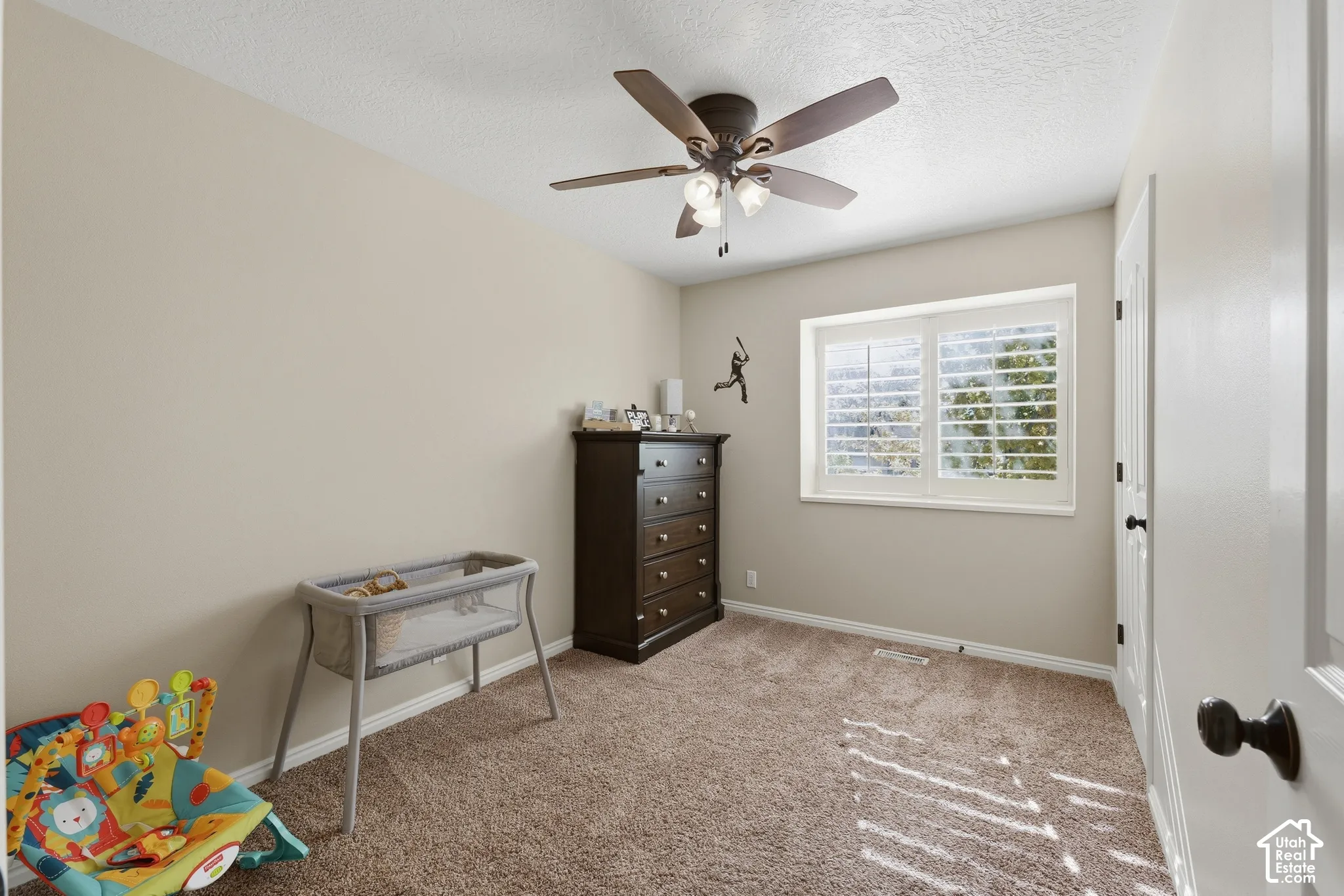 Neutral wall tones paired with carpeted flooring, window featuring interior plantation shutters, and a ceiling-mounted fan with integrated light fixture