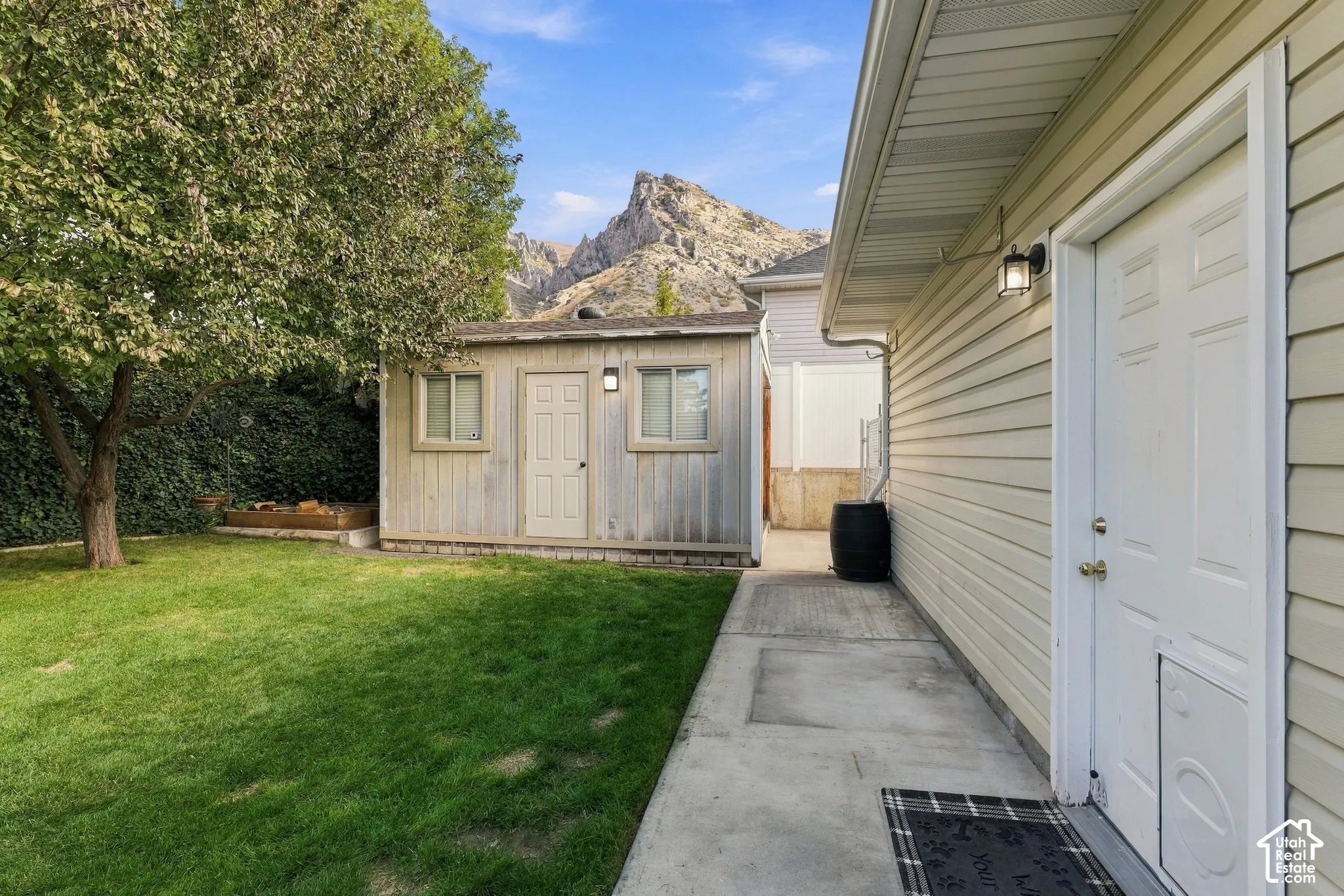 Backyard featuring a detached storage structure, concrete walkway, mature tree, and mountain backdrop
