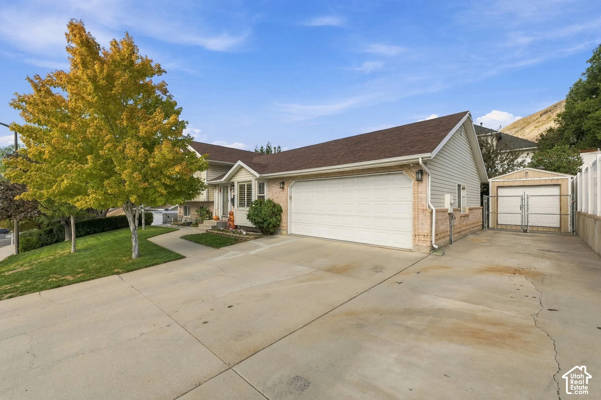 Exterior facade featuring light-colored horizontal siding and brick accents, an attached two-car garage, concrete driveway, and a detached storage shed