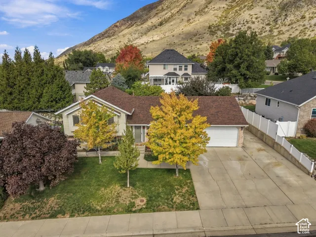 Single-level exterior featuring a multi-gabled asphalt shingle roof, integrated two-car garage, front-facing lawn with mature deciduous trees, and a mountain backdrop