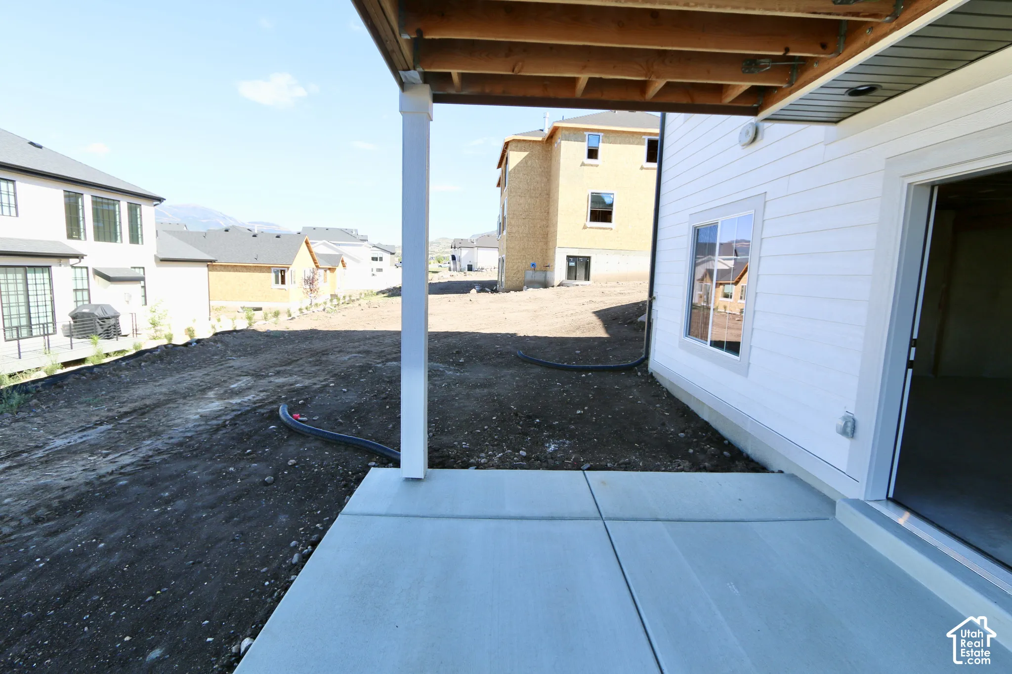 Covered concrete patio featuring white horizontal siding, exposed timber ceiling joists, and a sliding glass door