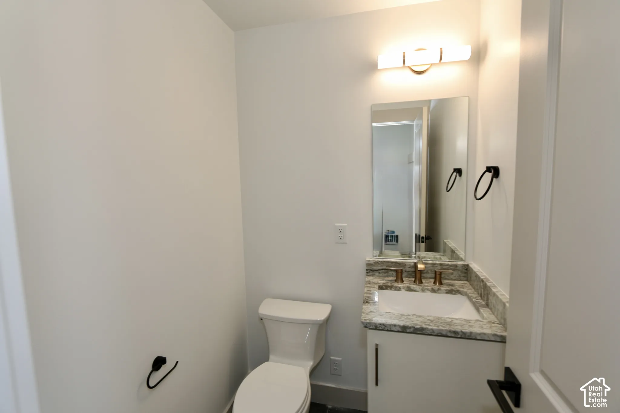 Stone-surface vanity featuring an integrated basin, contemporary wall-mounted light fixture, mirror, matte black hardware, and an elongated toilet