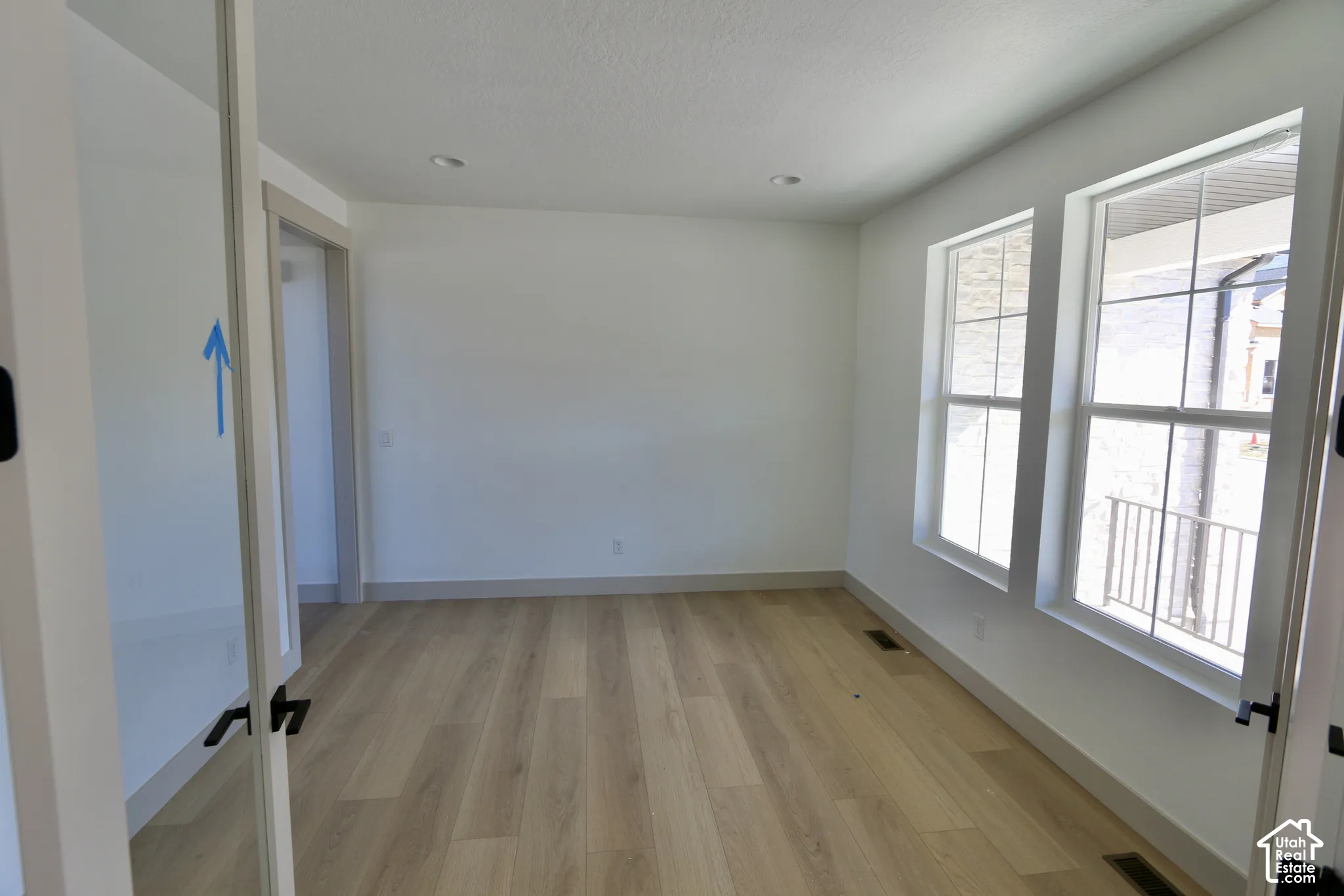 Interior space featuring light-toned wood-finish flooring, dual windows with muntin detailing, recessed lighting, and a glass-paneled entry door with matte black hardware
