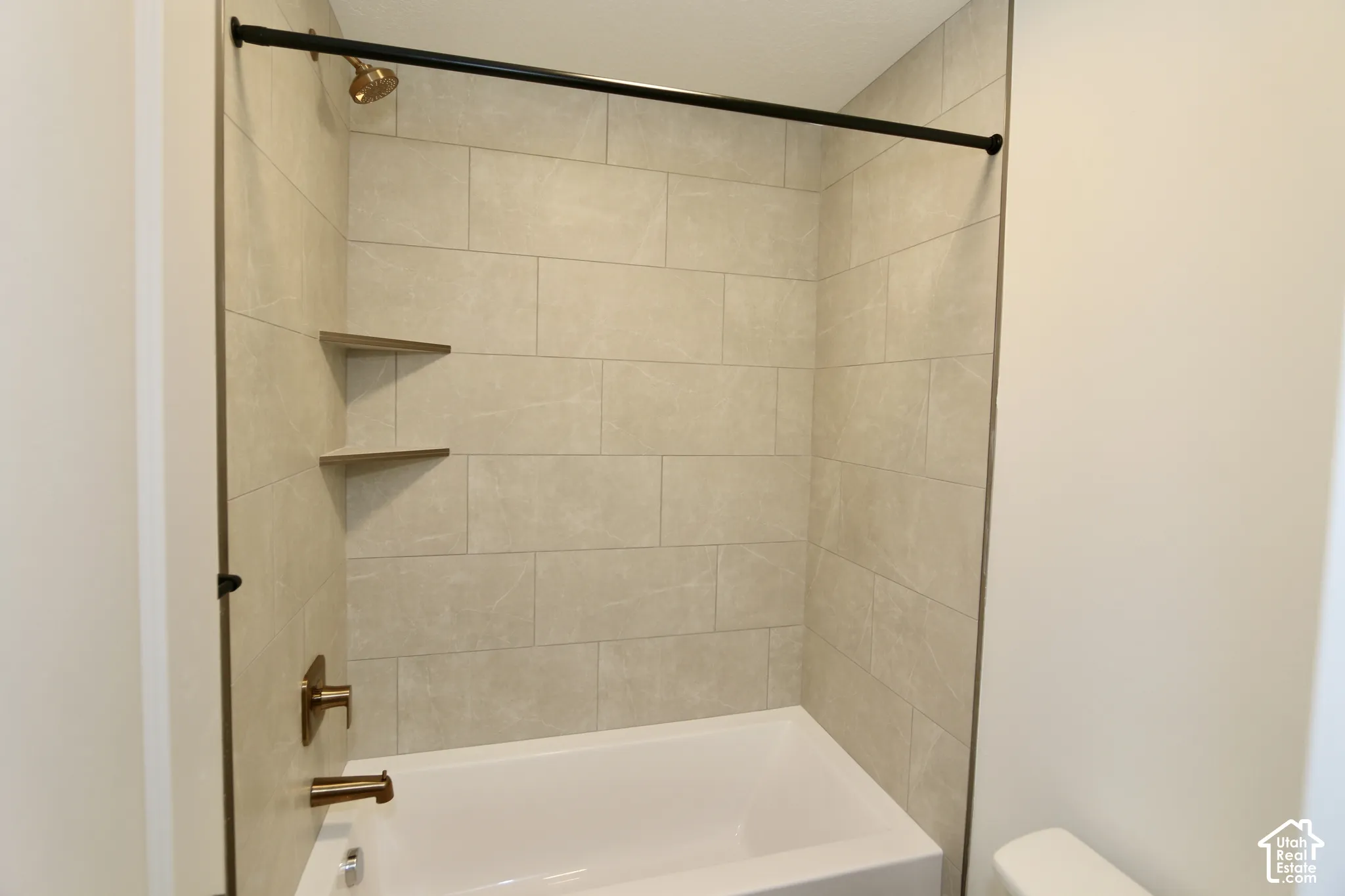 Bathroom #3 with Tub and shower surround featuring large-format neutral tile, built-in corner shelving, bronze-finish fixtures, and a matte black shower rod