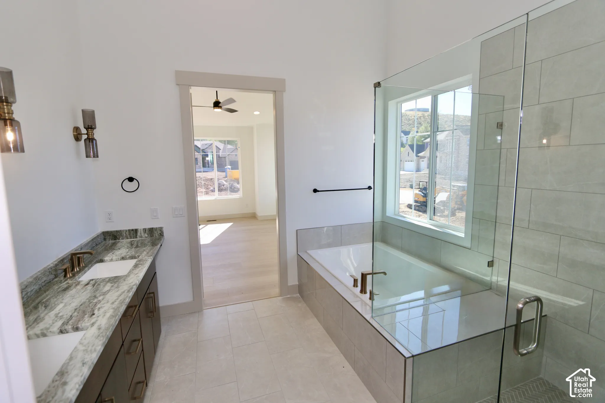 Dual-sink vanity with stone countertop and metallic fixtures, soaking tub with tile surround, glass-enclosed shower, and tile flooring