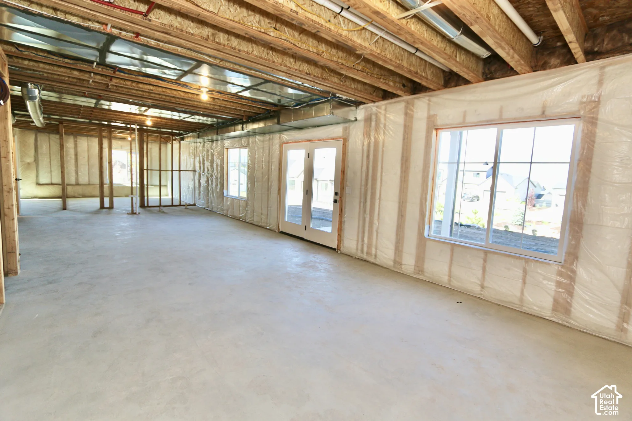 Unfinished basement featuring concrete flooring, exposed wood-frame ceiling joists, white-framed windows, and double glass-pane doors