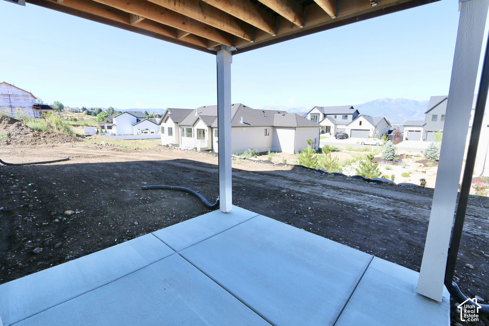 Covered patio featuring a concrete slab floor, exposed wood joists, and vertical support columns, opening to an expansive lot with a mountain backdrop