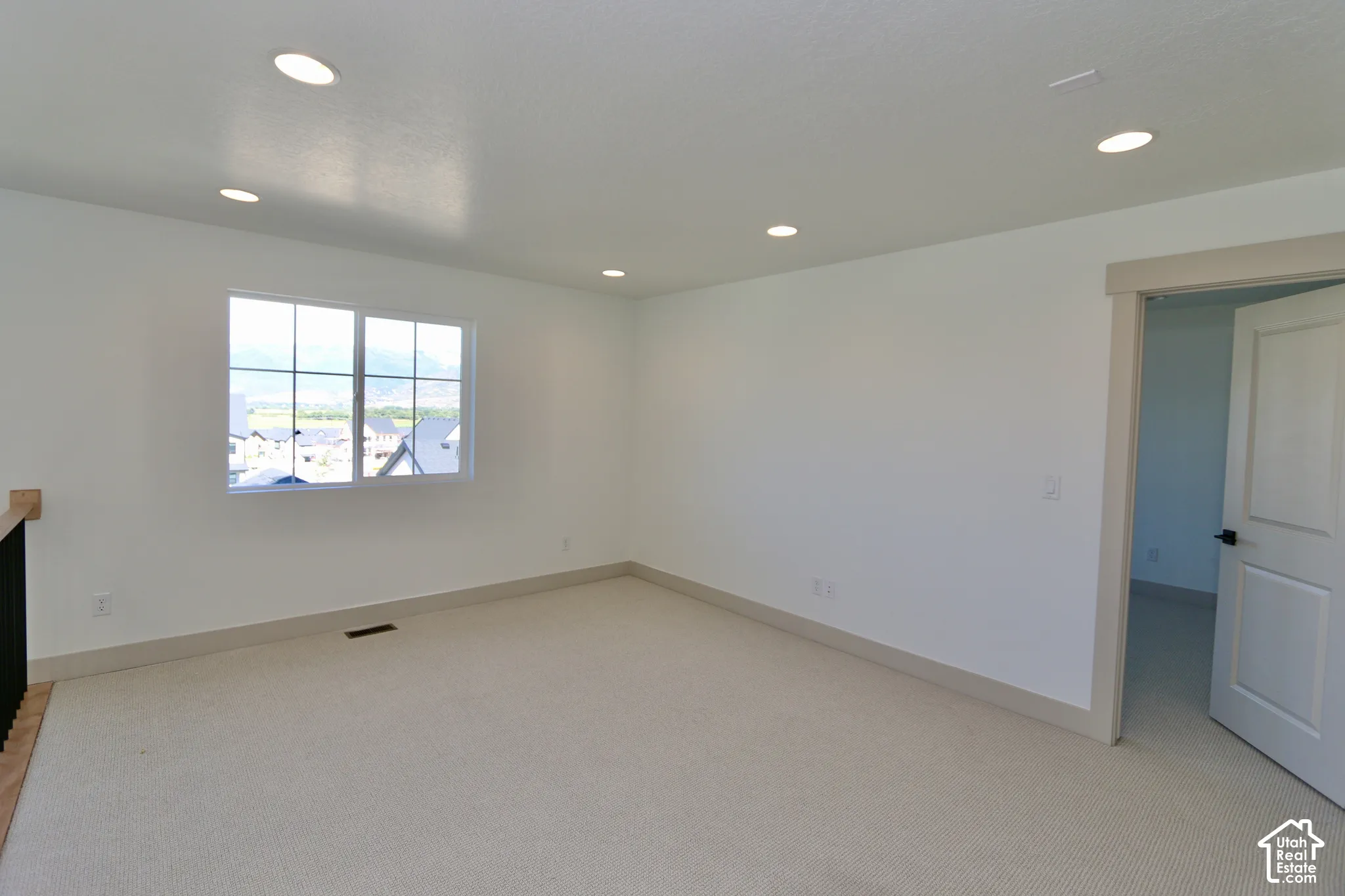 Spacious loft open to the greatroom below featuring neutral carpeting, recessed lighting, white walls, and a large window with windowpane muntins