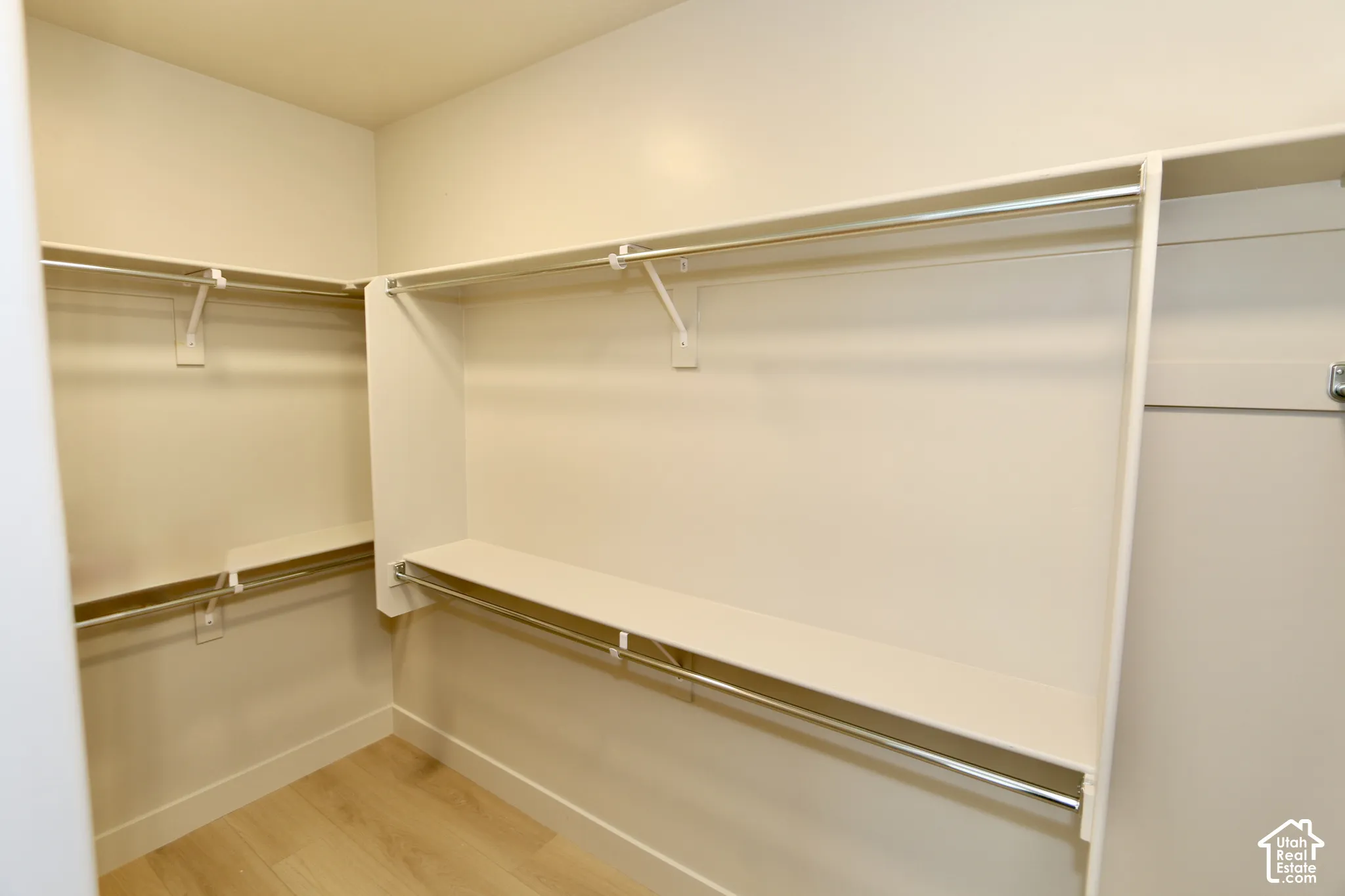 Master walk-in closet featuring multi-level white shelving, integrated metal clothing rods, and wood-finish flooring