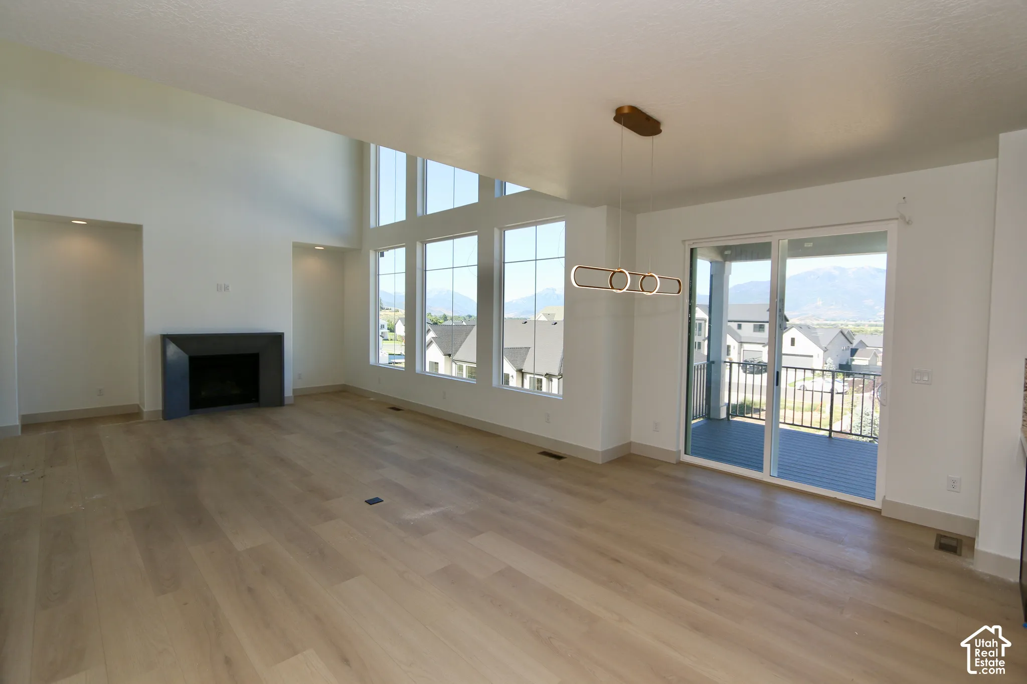 Open-concept interior featuring tall ceilings, wood-finish flooring, a modern geometric light fixture, a minimalist fireplace, and large windows with mountain scenery