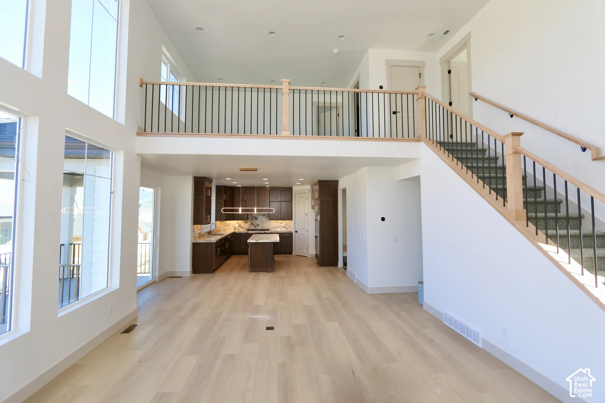 Open-concept interior featuring wood-finish flooring, floor-to-ceiling windows, a staircase with wood handrails and metal balusters, and a kitchen equipped with dark cabinetry and a center island