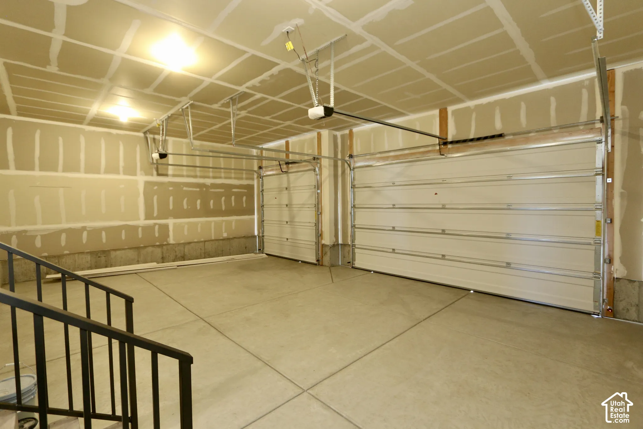 Multi-bay garage featuring concrete flooring, two overhead roll-up doors, ceiling-mounted automatic openers, and exposed drywall partitions