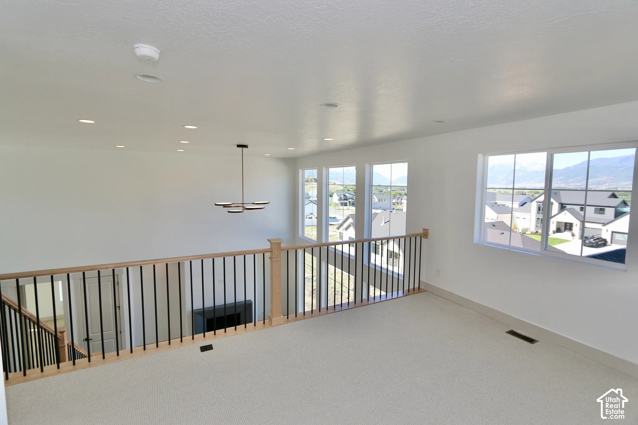 Open loft area featuring recessed lighting, a modern multi-arm chandelier, large windows with mountain scenery, and a wood-capped railing with vertical metal balusters