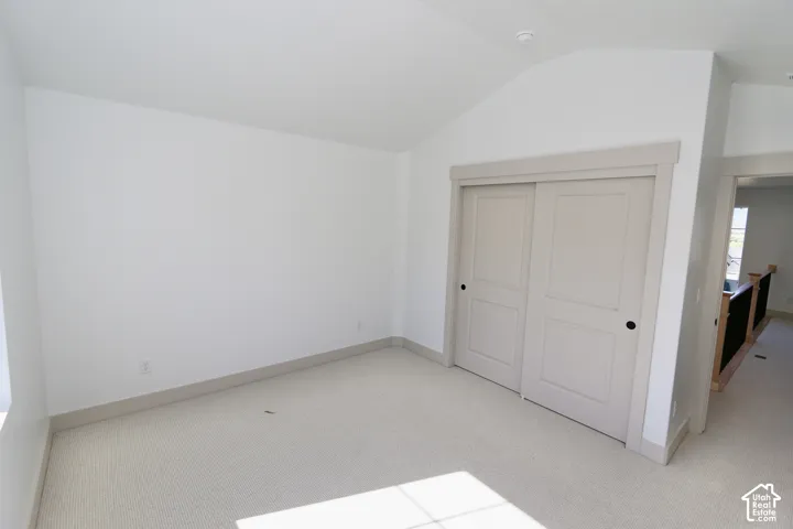 Room with a vaulted ceiling, neutral wall-to-wall carpeting, and sliding panel closet doors with matching trim