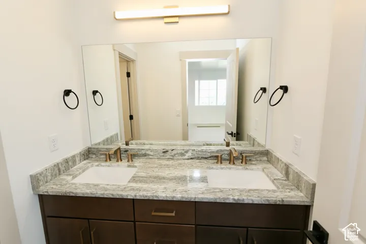 Bathroom $3 with Double-sink vanity featuring stone-surfaced countertop, integrated rectangular basins, dark-finish cabinetry, metallic fixtures, and wall-mounted lighting