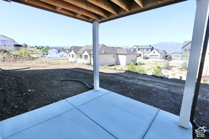 Covered patio featuring a concrete slab floor, exposed wood joists, and vertical support columns, opening to an expansive lot with a mountain backdrop