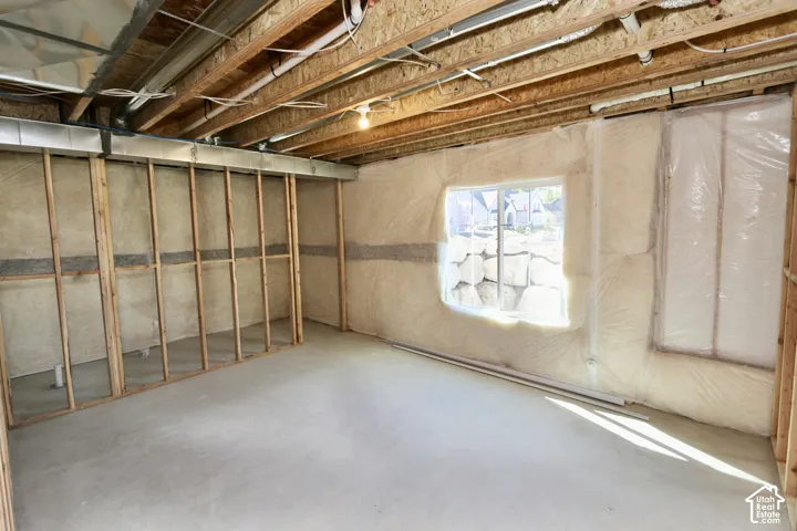 Unfinished space featuring concrete flooring, exposed wooden ceiling joists, wood-framed stud walls, and insulated wall panels with a single window