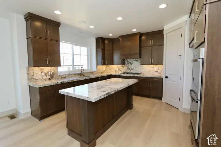 Kitchen featuring dark wood cabinetry, a central island with stone countertops, a full-height stone backsplash, recessed lighting, and wood-finish flooring