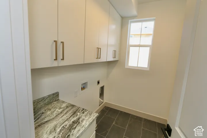 Laundry area featuring white cabinetry with metallic pulls, stone countertop, large-format tile flooring, and a single-hung window