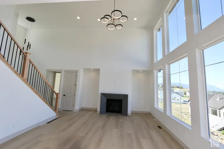 Two-story living area featuring vaulted ceilings, floor-to-ceiling windows, wood-finish flooring, a contemporary fireplace, and a sculptural multi-ring chandelier