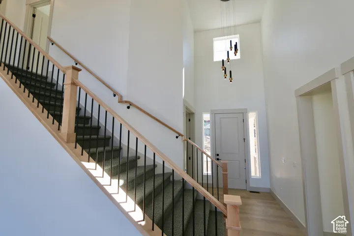 Two-story foyer featuring high ceilings, a natural wood-finish handrail, vertical metal balusters, carpeted stairs, and a multi-pendant light fixture
