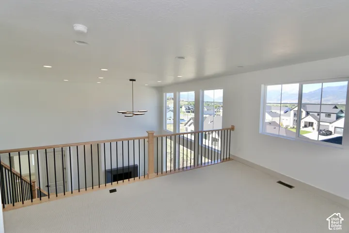 Open loft area featuring recessed lighting, a modern multi-arm chandelier, large windows with mountain scenery, and a wood-capped railing with vertical metal balusters