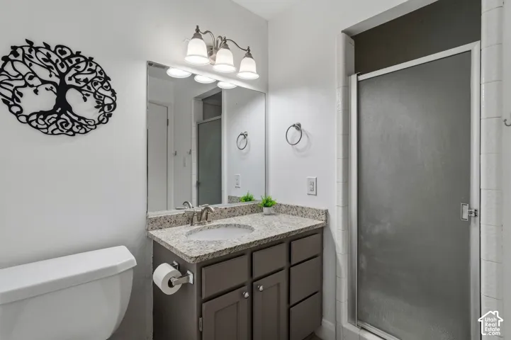 Bathroom featuring a stone-composite countertop with an integrated oval sink, dark-toned cabinetry, a wall-to-wall vanity mirror, three-light fixture, and a shower enclosure with a frosted glass door