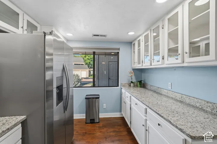 Kitchen featuring white cabinetry with glass-front uppers, speckled stone countertops, wood-finish flooring, recessed lighting, and stainless steel side-by-side refrigerator