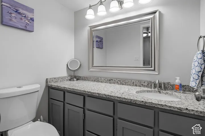 Bathroom featuring grey shaker-style cabinetry, speckled stone countertop, integrated oval undermount sink, brushed-nickel faucet, and a large framed vanity mirror with four-light fixture
