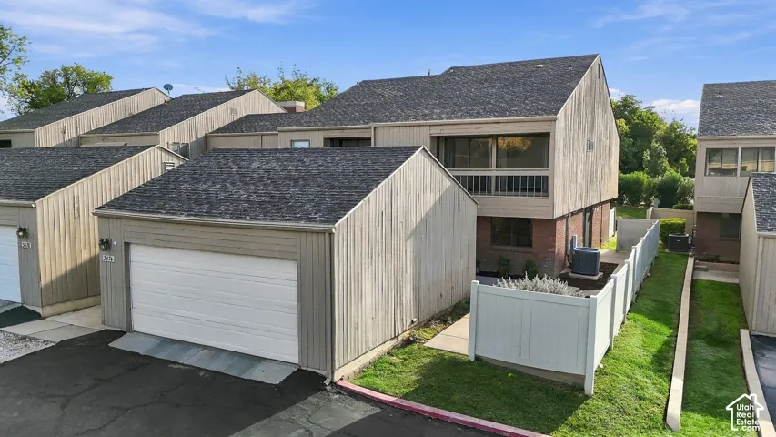 Multi-level exterior featuring vertical wood-finish siding, brick masonry, asphalt shingle roofing, an attached garage, and an enclosed patio area