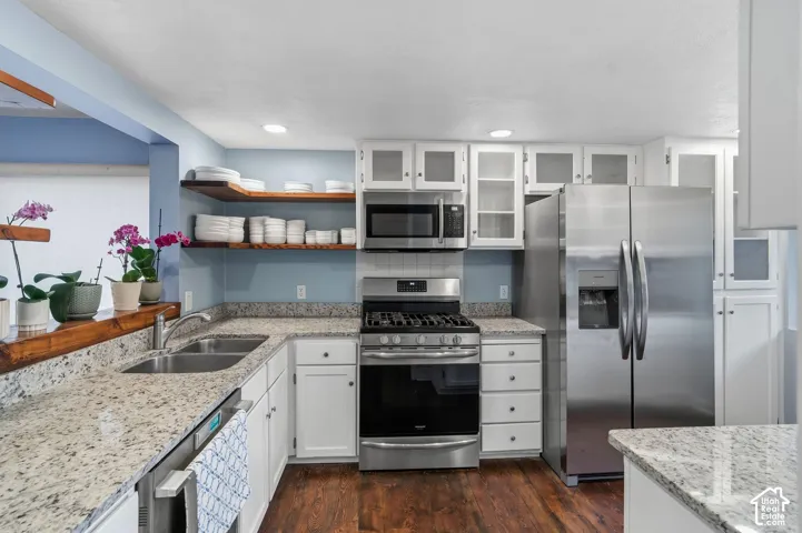 Kitchen featuring stone countertops, stainless steel appliances, white cabinetry with glass-front uppers, open wood shelving, and wood-finish flooring