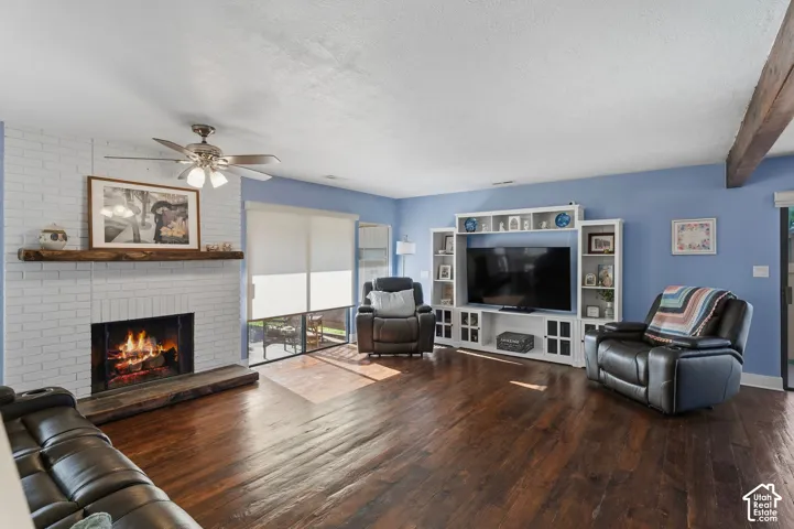 Living area featuring wood-finish flooring, a painted brick fireplace with a natural wood mantel, built-in shelving cabinetry, and a ceiling fan