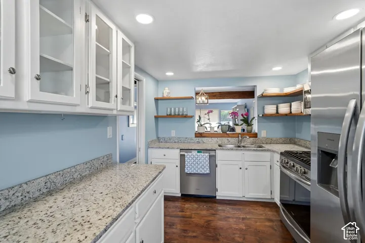 Kitchen featuring white cabinetry with glass-front uppers, speckled stone countertops, stainless steel appliances, open wood shelving, and wood-finish flooring