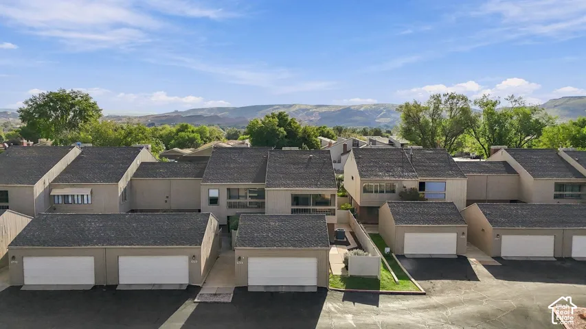 Multi-family residential complex featuring asphalt shingle roofs, stucco exterior siding, private garage bays, and mountain backdrop