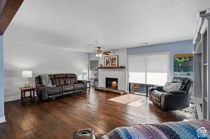 Living area featuring wood-finish flooring, a painted brick accent wall, and a fireplace with a natural wood mantel