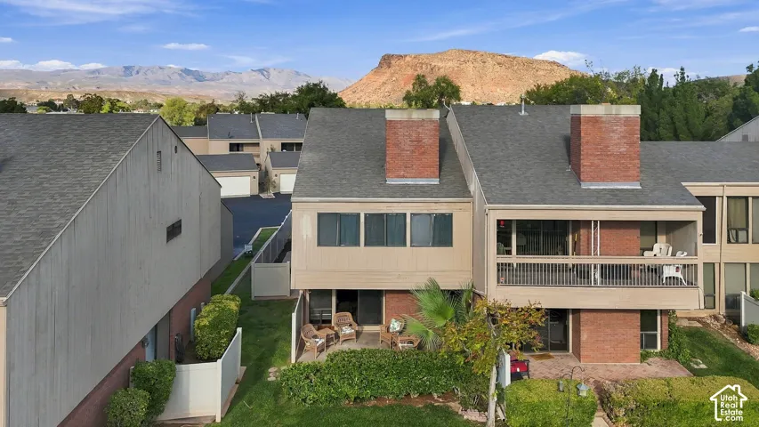 Multi-level exterior featuring dual brick chimneys, private second-story balcony with metal railing, ground-level patio, and mountain backdrop