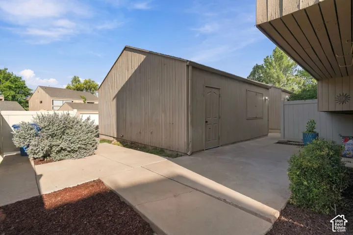 Exterior storage shed featuring vertical siding, a solid entry door, and a dedicated concrete patio area enclosed by privacy fencing