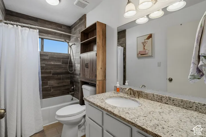 Bathroom featuring a vanity with a stone-finish countertop, wood-finish tile shower surround, integrated wooden cabinetry, and five-light vanity fixture