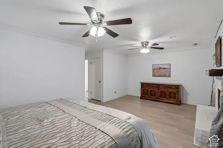 Wood-finish flooring, dual ceiling fans with integrated lighting, crown molding, and a painted brick fireplace hearth