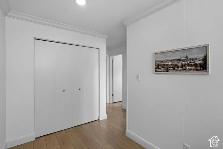 Hallway featuring wood-finish flooring, white walls, crown molding, and a bi-fold closet door