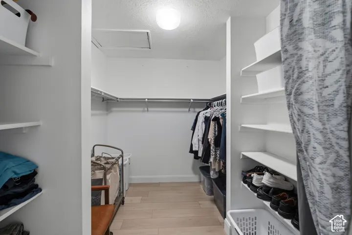 Walk-in closet featuring white built-in shelving, wood-finish flooring, ceiling-mounted lighting, and metal clothes rods