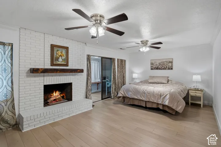 Painted brick fireplace featuring a rustic timber mantel, wood-finish flooring, and dual ceiling fans with integrated light fixtures
