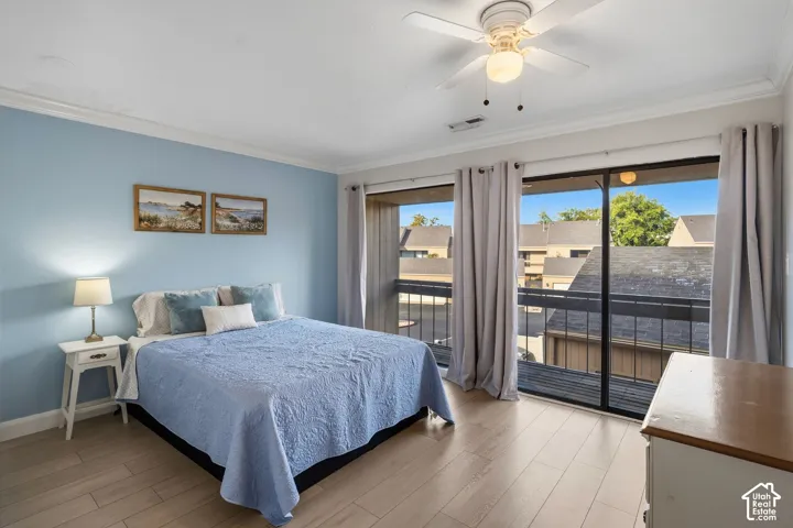 Sliding glass doors opening to a private balcony with metal railing, wood-finish flooring, ceiling fan with integrated lighting, and crown molding