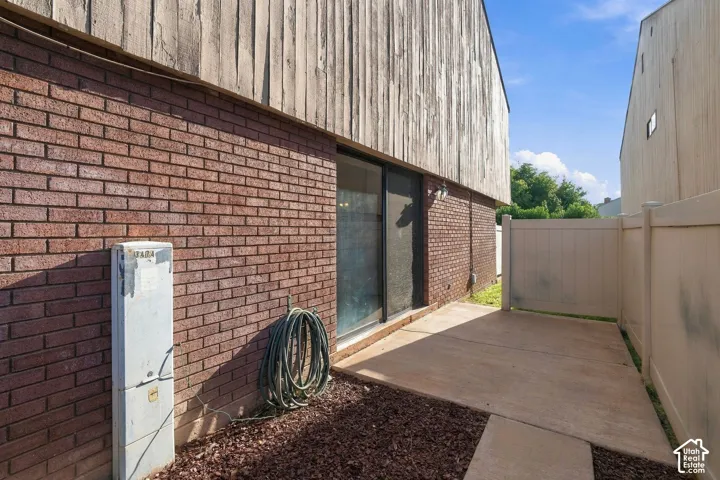 Exterior elevation featuring red brick masonry, vertical wood-panel siding, a concrete patio, and a vinyl privacy fence