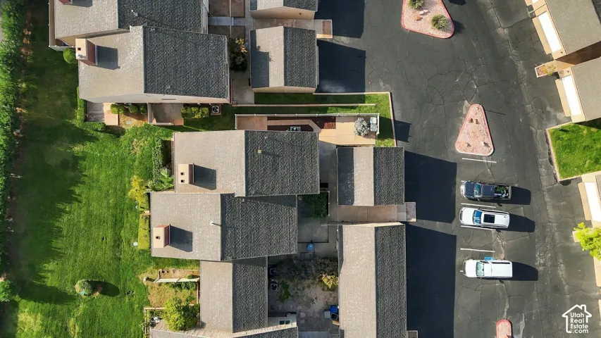 Aerial perspective of property featuring shingle roofing, private hardscaped outdoor patio areas, and access to paved surface parking