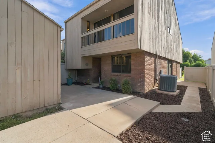 Exterior featuring a vertical wood-sided upper level, brick masonry, a covered balcony, a private concrete patio, and fenced perimeter